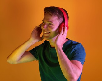 Photo of Smiling man wearing headphones listening to music in neon lights against orange background