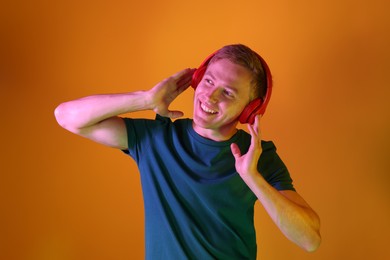 Photo of Smiling man wearing headphones listening to music in neon lights against orange background