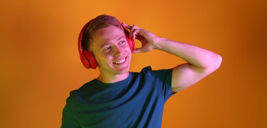 Photo of Smiling man wearing headphones listening to music in neon lights against orange background