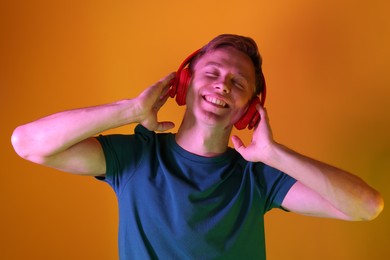 Photo of Smiling man wearing headphones listening to music in neon lights against orange background