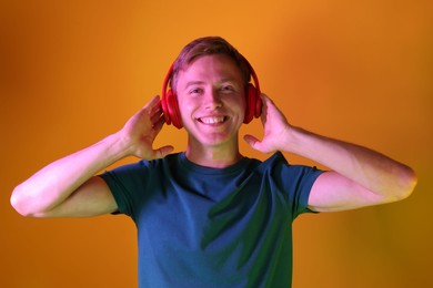 Photo of Smiling man wearing headphones listening to music in neon lights against orange background