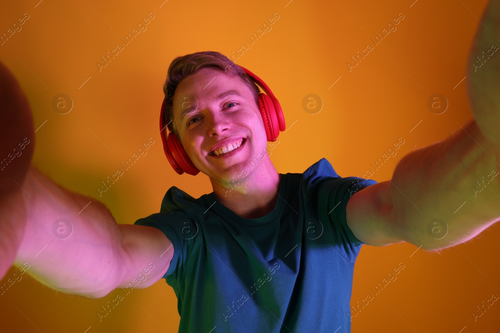 Smiling man wearing headphones taking selfie in neon lights against orange background Photo of Smiling man wearing headphones taking selfie in neon lights against orange background