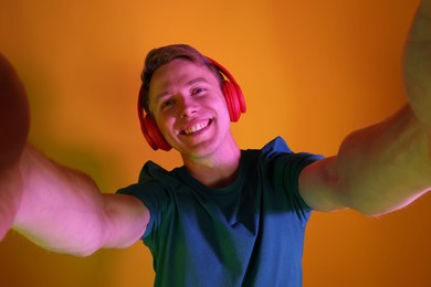 Photo of Smiling man wearing headphones taking selfie in neon lights against orange background