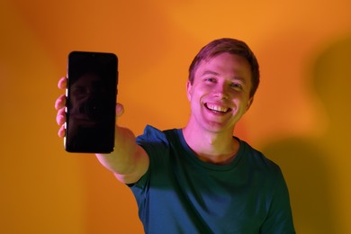 Photo of Happy man showing smartphone in neon lights against orange background