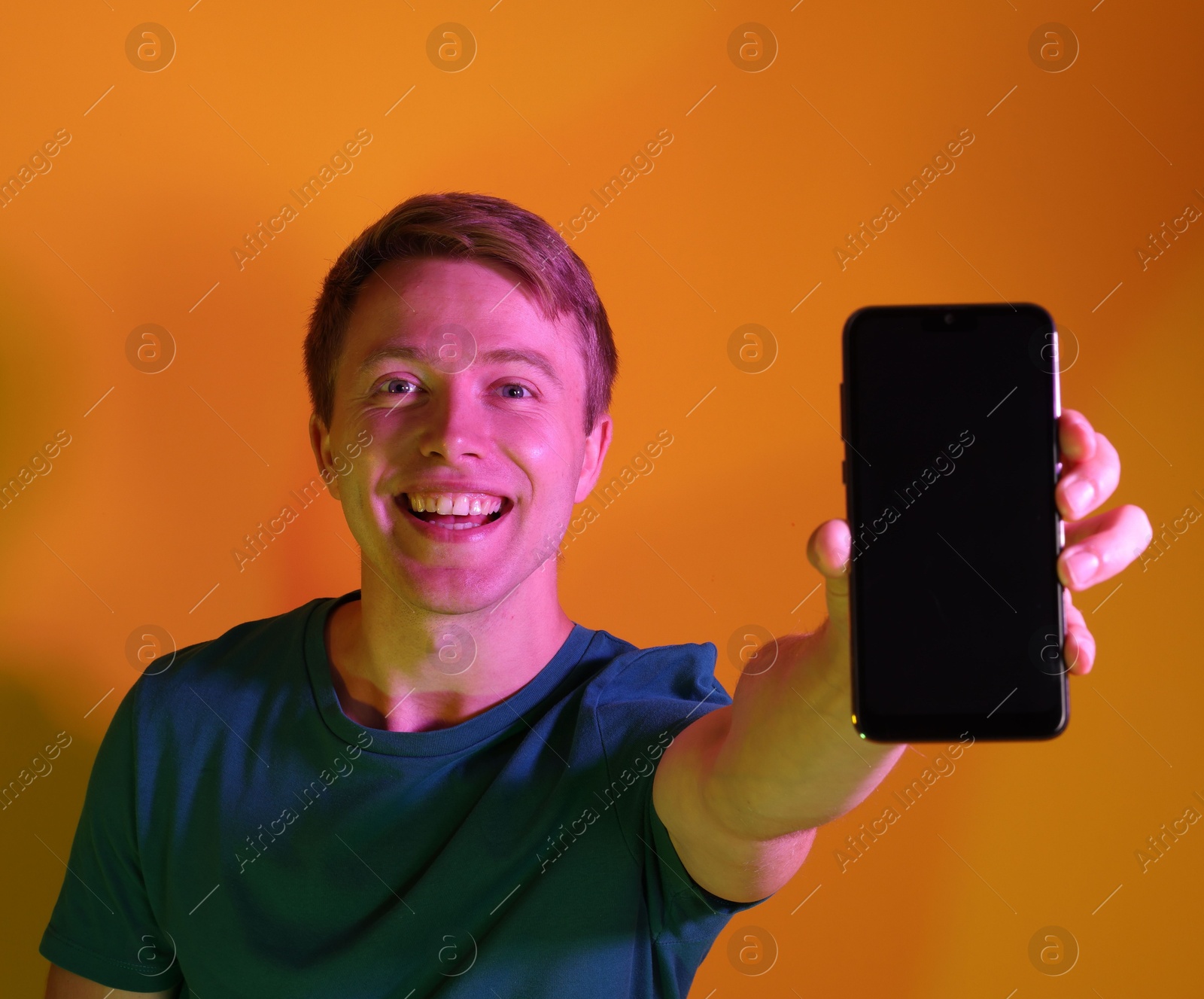 Happy man showing smartphone in neon lights against orange background Photo of Happy man showing smartphone in neon lights against orange background