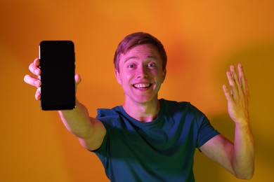 Photo of Happy man showing smartphone in neon lights against orange background