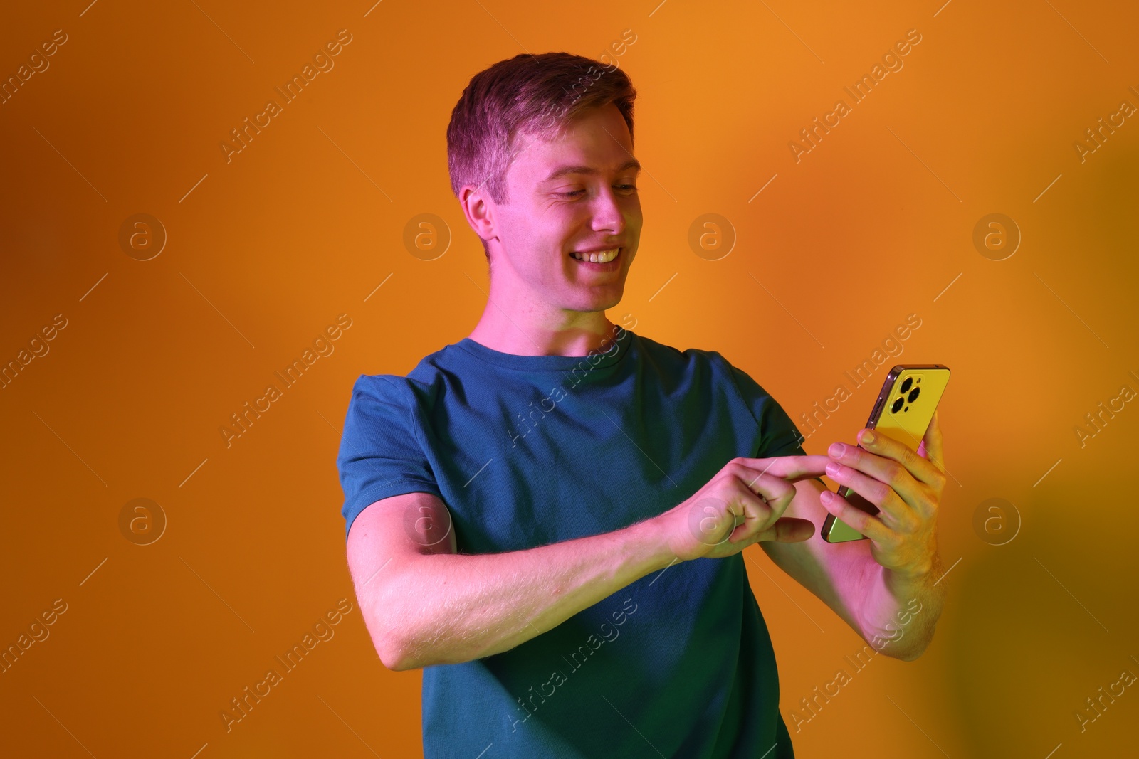 Happy man using smartphone in neon lights against orange background Photo of Happy man using smartphone in neon lights against orange background