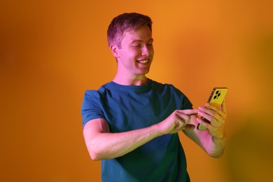 Photo of Happy man using smartphone in neon lights against orange background