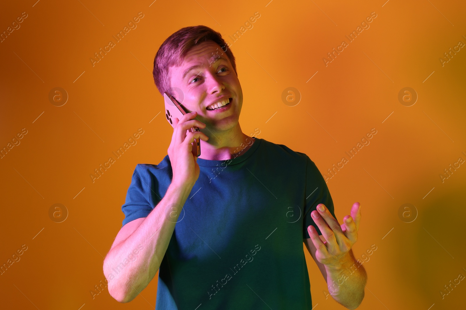 Happy man talking on smartphone in neon lights against orange background Photo of Happy man talking on smartphone in neon lights against orange background