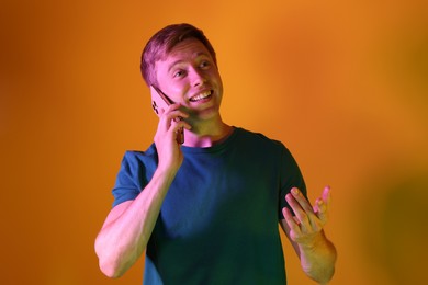 Photo of Happy man talking on smartphone in neon lights against orange background