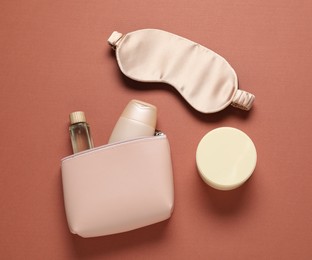 Photo of Bag with cosmetic products and sleeping mask on brown background, flat lay