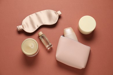 Photo of Bag with cosmetic products and sleeping mask on brown background, flat lay