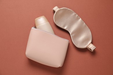Photo of Bag with cosmetic product and sleeping mask on brown background, flat lay