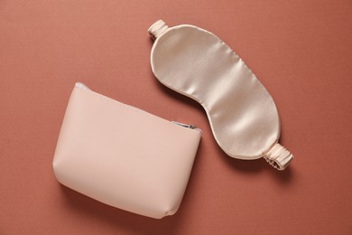Photo of Cosmetic bag and sleeping mask on brown background, flat lay