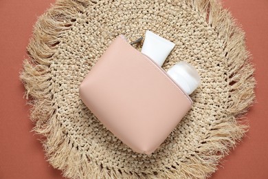 Photo of Bag with cosmetic products and wicker mat on brown background, top view