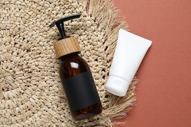 Photo of Cosmetic products and wicker mat on brown background, flat lay. Mockup for design