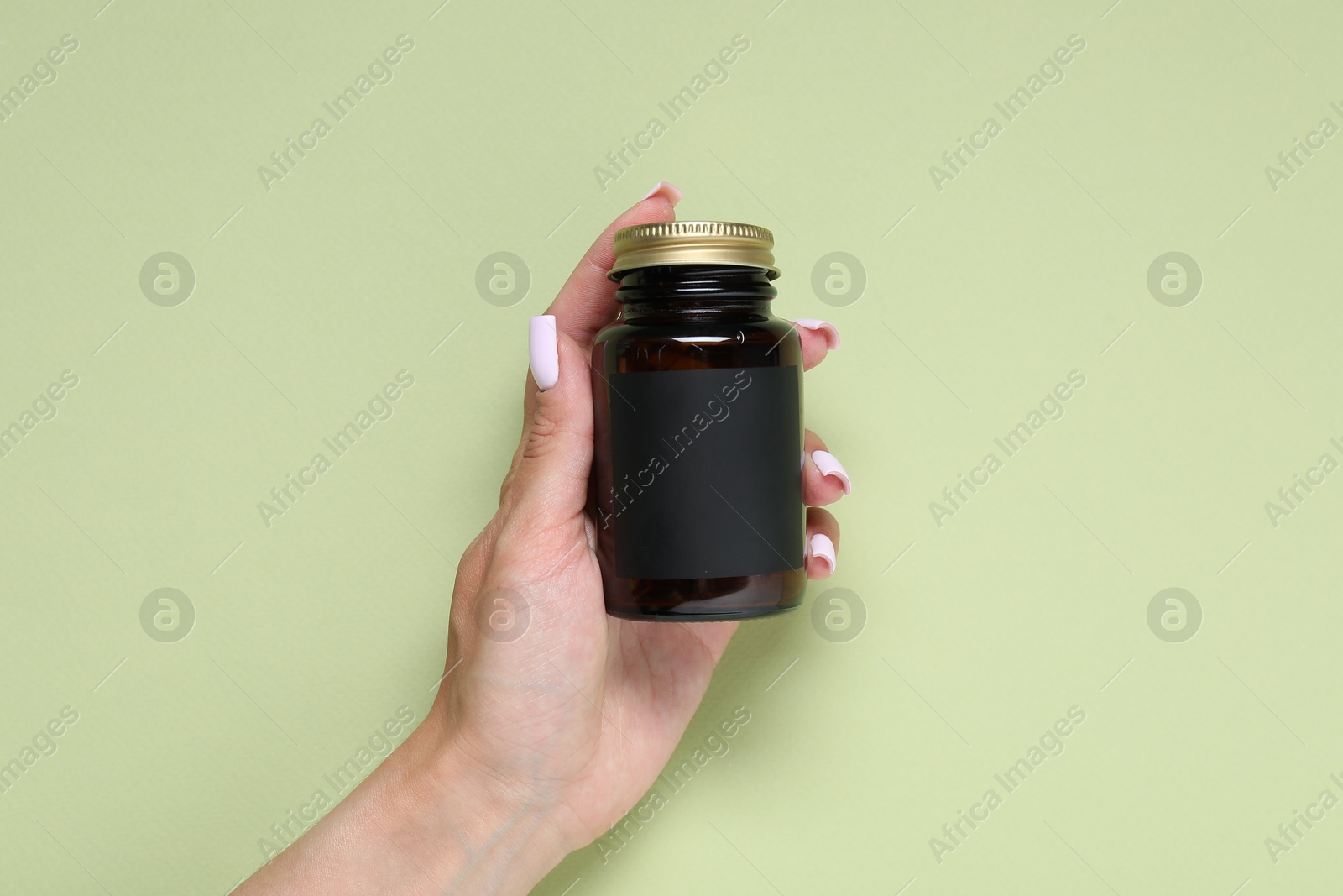 Woman with jar of vitamins on light green background, closeup Photo of Woman with jar of vitamins on light green background, closeup