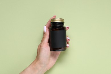 Photo of Woman with jar of vitamins on light green background, closeup