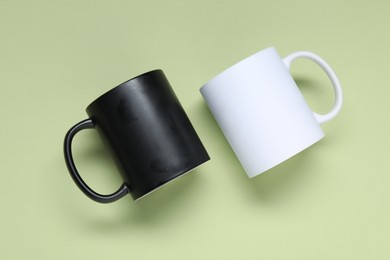 Photo of Mugs on light green background, top view. Mockup for design