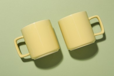Photo of Yellow mugs on light green background, top view. Mockup for design
