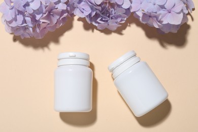 Photo of Jars of vitamins and flowers on beige background, flat lay