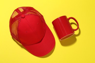 Photo of Red mug and cap on yellow background, flat lay. Mockup for design