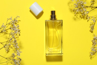Photo of Bottle of perfume and flowers on yellow background, flat lay
