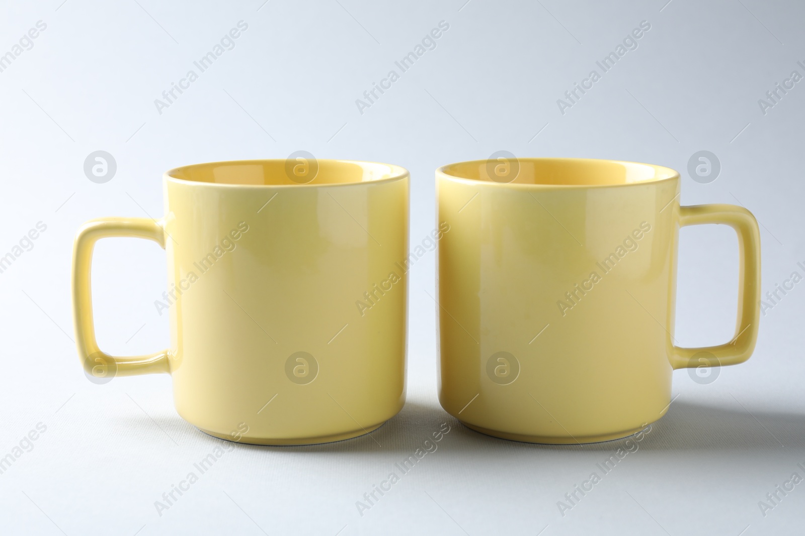 Yellow mugs on light background. Mockup for design Photo of Yellow mugs on light background. Mockup for design