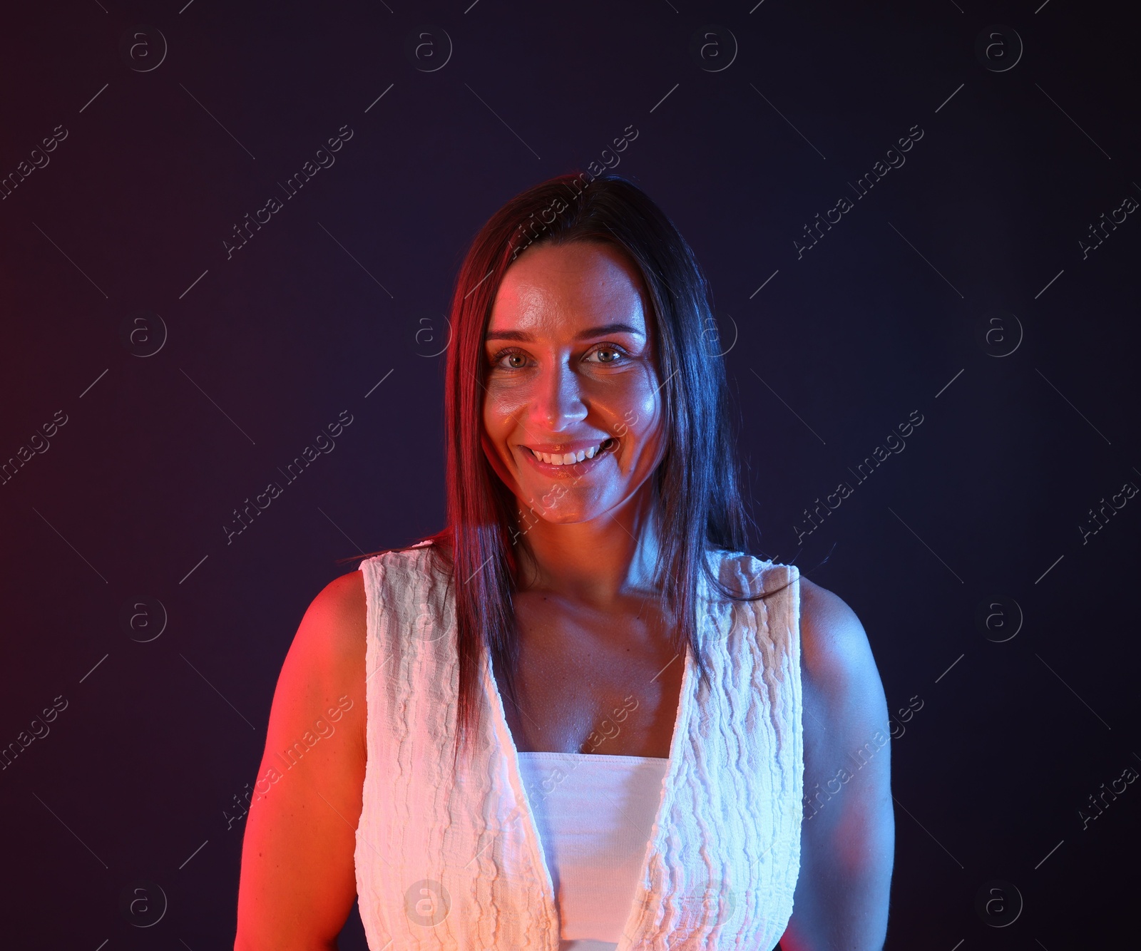 Portrait of smiling woman in neon lights against dark background Photo of Portrait of smiling woman in neon lights against dark background