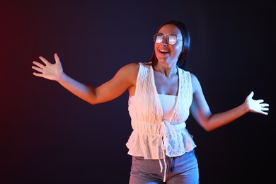 Photo of Smiling woman wearing sunglasses in neon lights against dark background