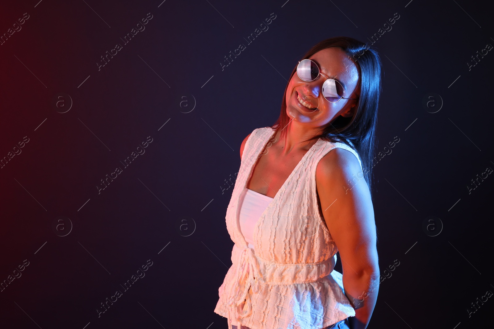 Happy woman wearing sunglasses in neon lights against dark background. Space for text Photo of Happy woman wearing sunglasses in neon lights against dark background. Space for text