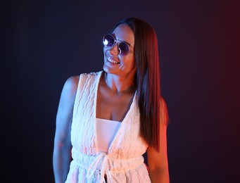 Photo of Smiling woman wearing sunglasses in neon lights against dark background