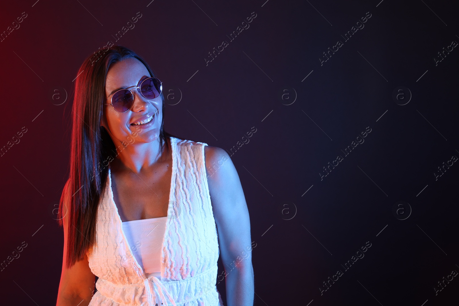 Happy woman wearing sunglasses in neon lights against dark background. Space for text Photo of Happy woman wearing sunglasses in neon lights against dark background. Space for text
