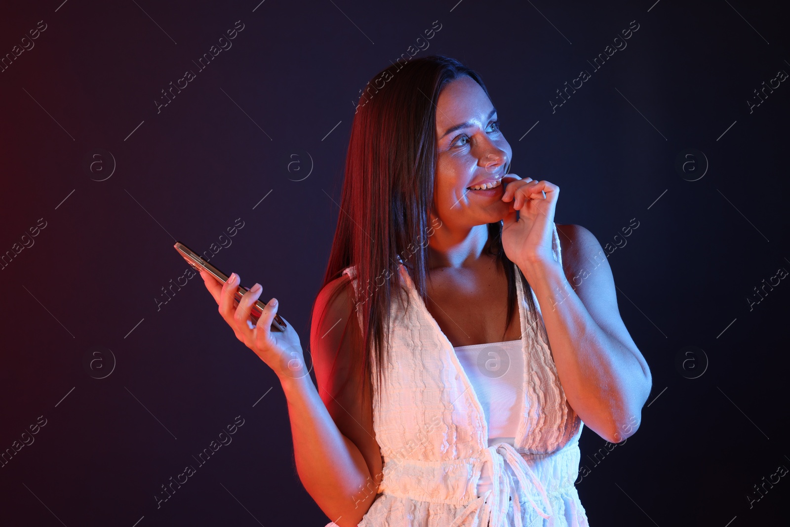 Happy woman with smartphone in neon lights against dark background Photo of Happy woman with smartphone in neon lights against dark background