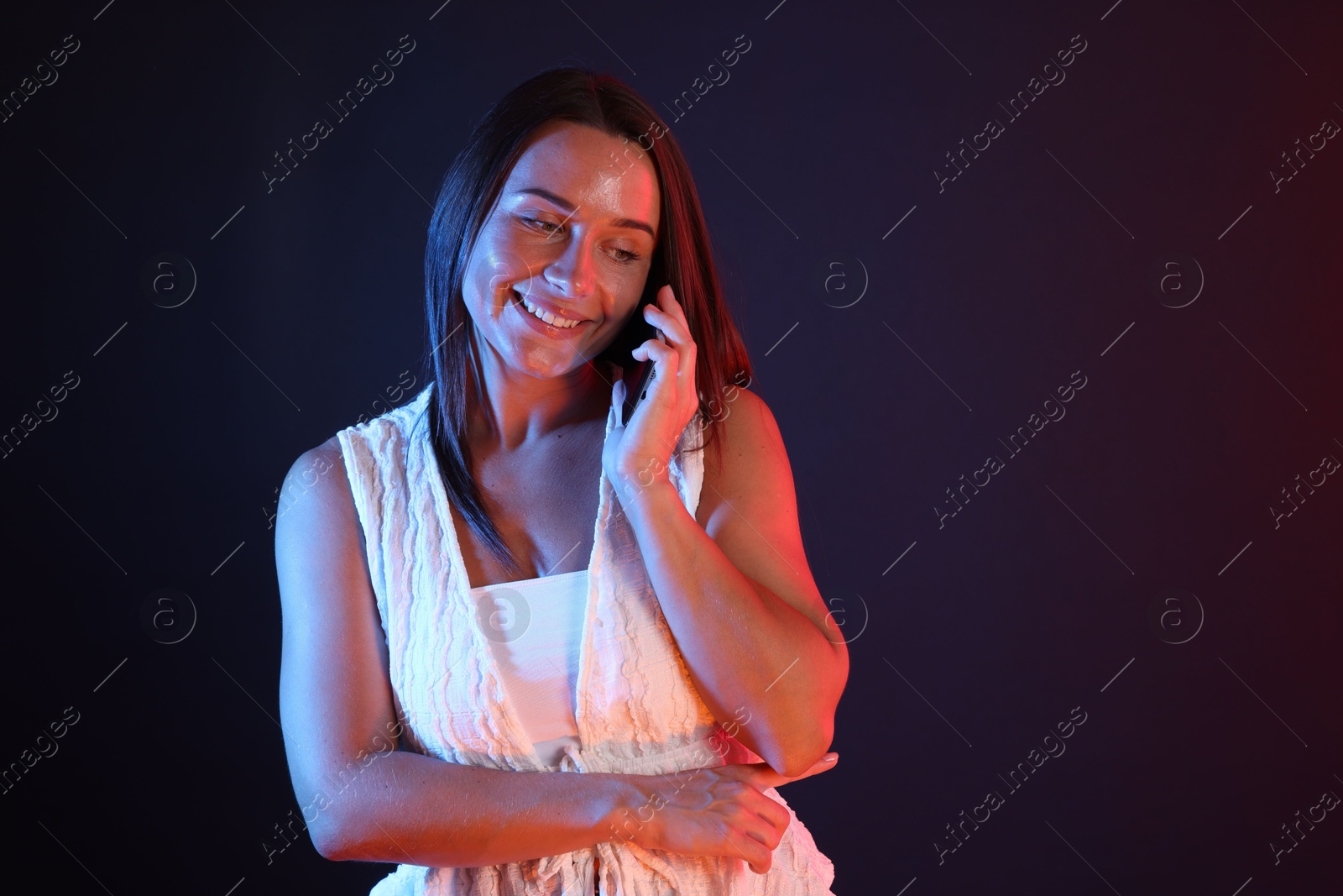 Happy woman talking by smartphone in neon lights against dark background Photo of Happy woman talking by smartphone in neon lights against dark background
