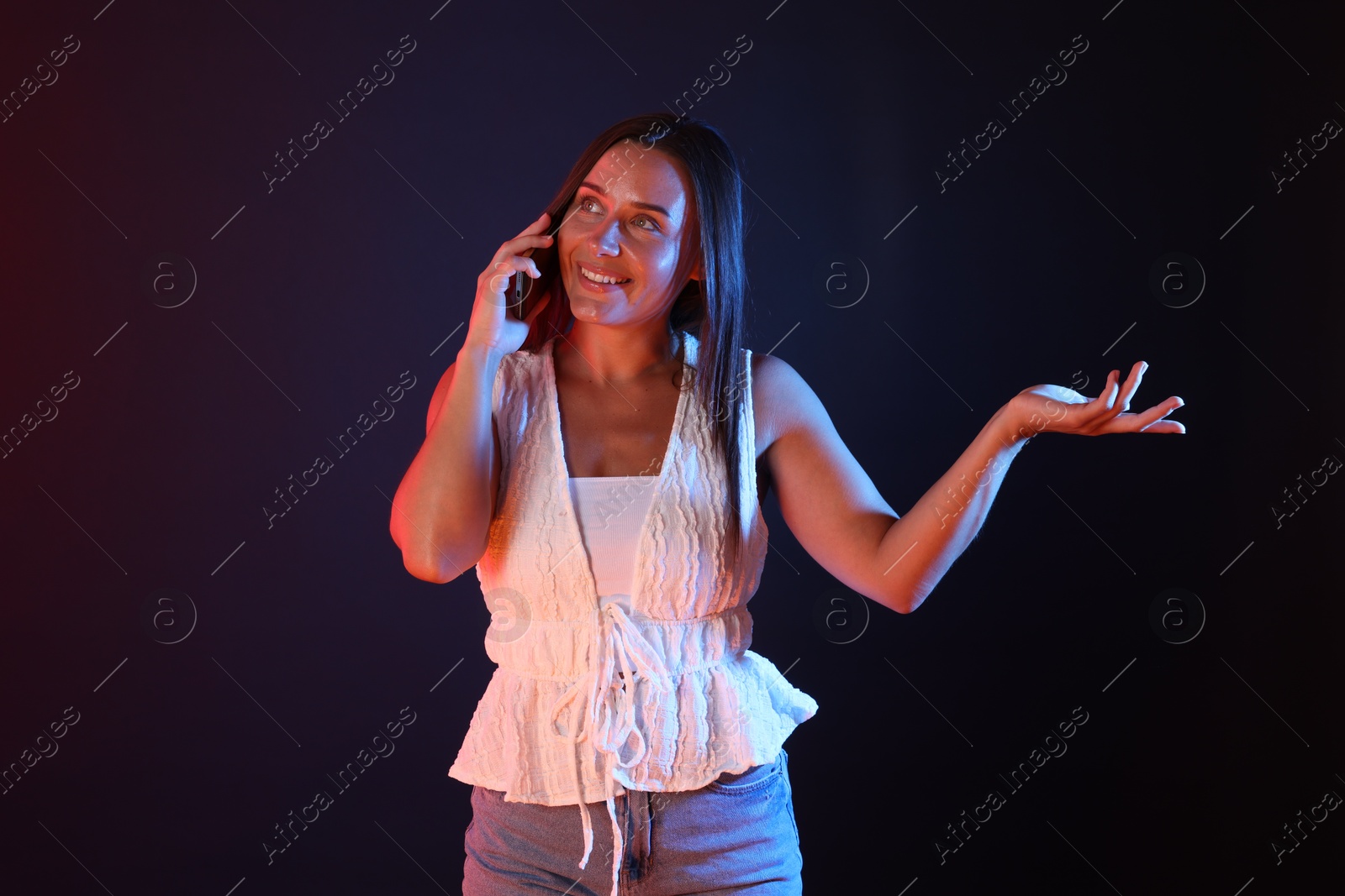 Happy woman talking by smartphone in neon lights against dark background Photo of Happy woman talking by smartphone in neon lights against dark background