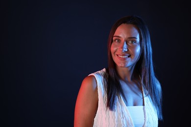 Photo of Smiling woman in neon lights against black background. Space for text