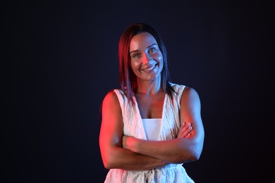 Photo of Portrait of smiling woman with crossed arms in neon lights against black background