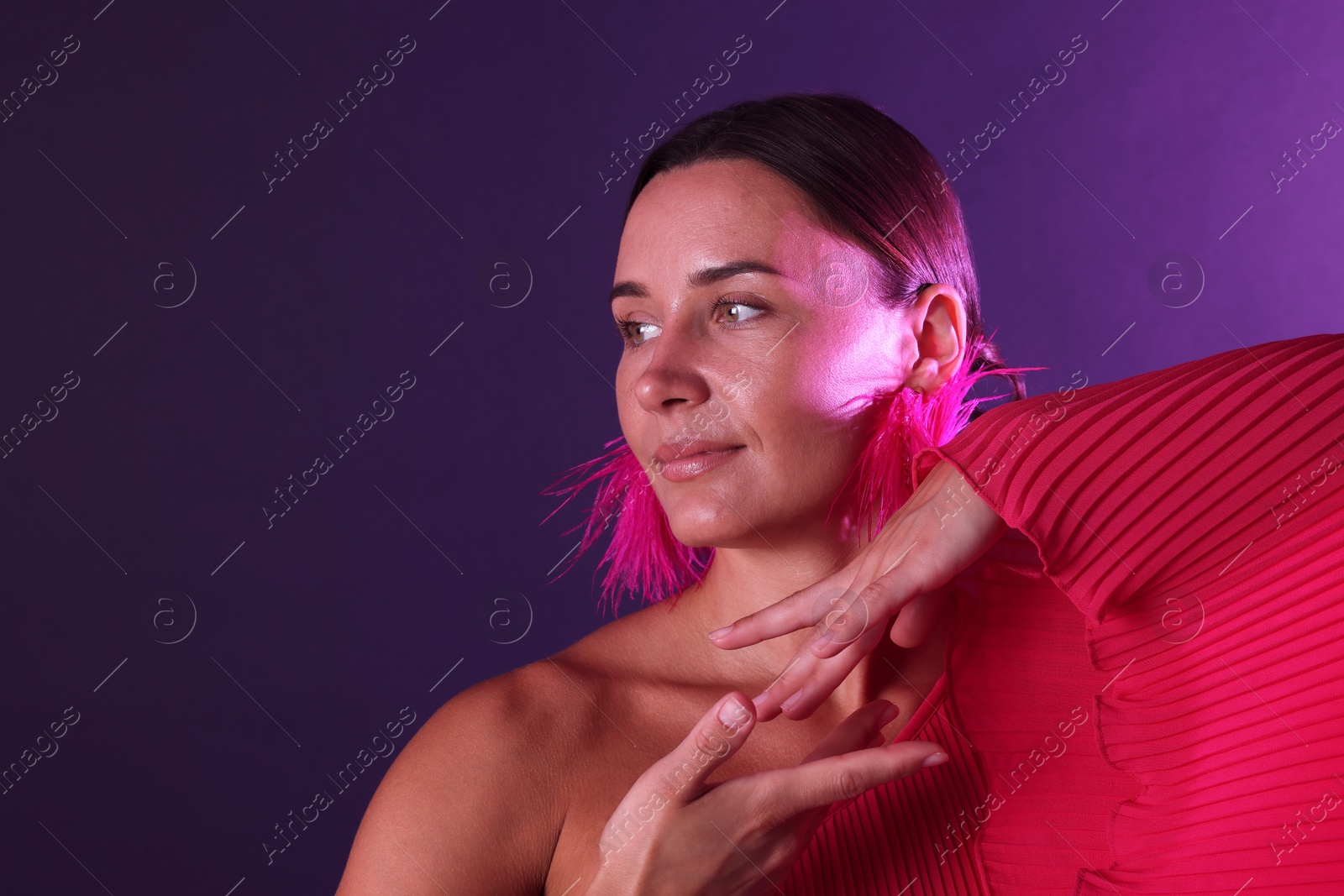 Beautiful woman wearing fur earrings in neon lights against purple background. Space for text Photo of Beautiful woman wearing fur earrings in neon lights against purple background. Space for text