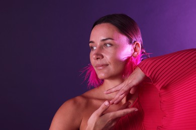 Photo of Beautiful woman wearing fur earrings in neon lights against purple background. Space for text