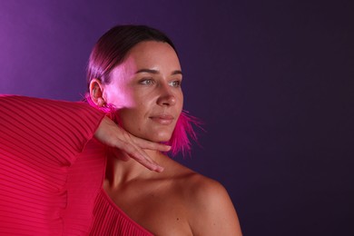 Photo of Beautiful woman wearing fur earrings in neon lights against purple background. Space for text