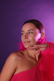 Photo of Beautiful woman wearing fur earrings in neon lights against purple background