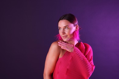 Photo of Beautiful woman wearing fur earrings in neon lights against purple background. Space for text