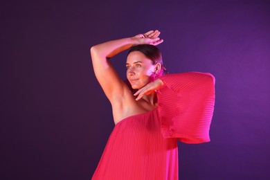 Photo of Beautiful woman wearing fur earrings in neon lights against purple background