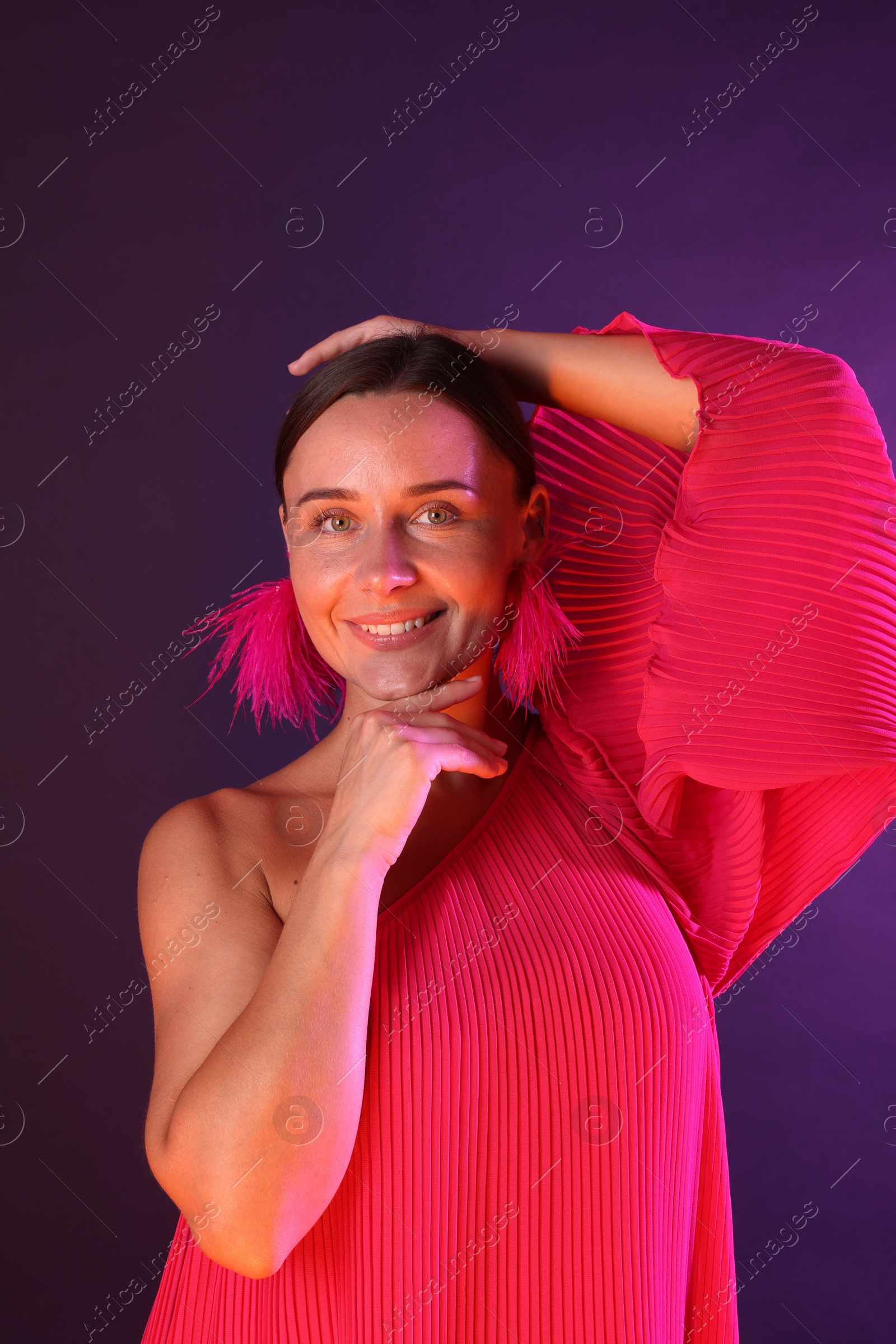 Portrait of smiling woman wearing fur earrings in neon lights against purple background Photo of Portrait of smiling woman wearing fur earrings in neon lights against purple background