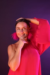 Photo of Portrait of smiling woman wearing fur earrings in neon lights against purple background