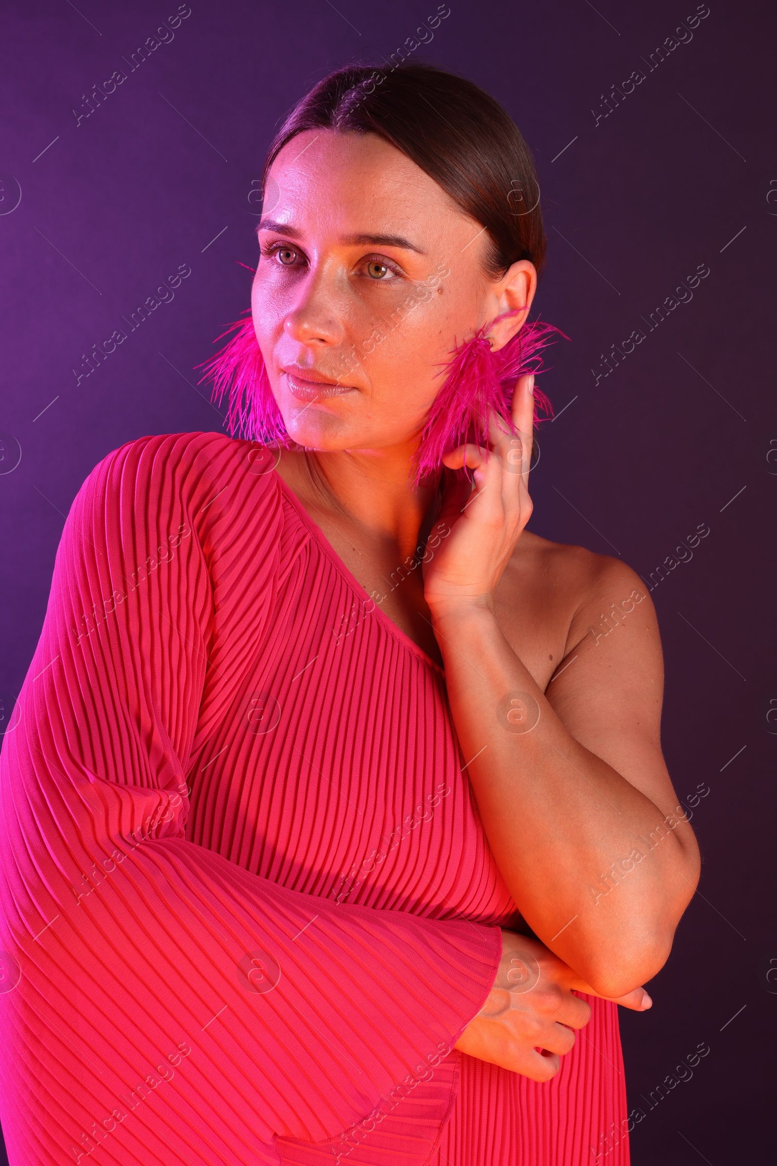 Beautiful woman wearing fur earrings in neon lights against purple background Photo of Beautiful woman wearing fur earrings in neon lights against purple background