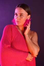 Photo of Beautiful woman wearing fur earrings in neon lights against purple background