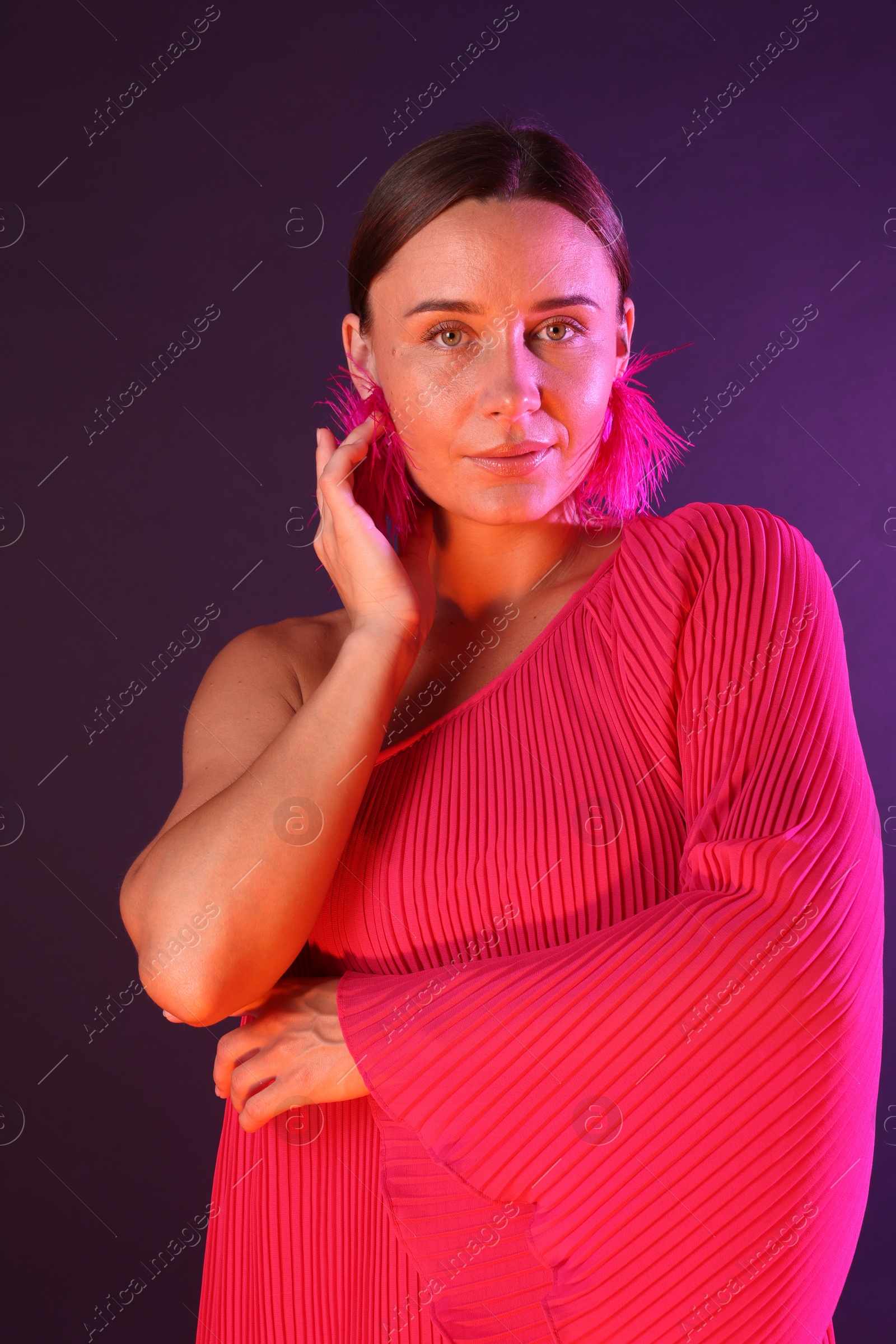 Portrait of beautiful woman wearing fur earrings in neon lights against purple background Photo of Portrait of beautiful woman wearing fur earrings in neon lights against purple background