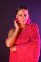 Photo of Portrait of beautiful woman wearing fur earrings in neon lights against purple background